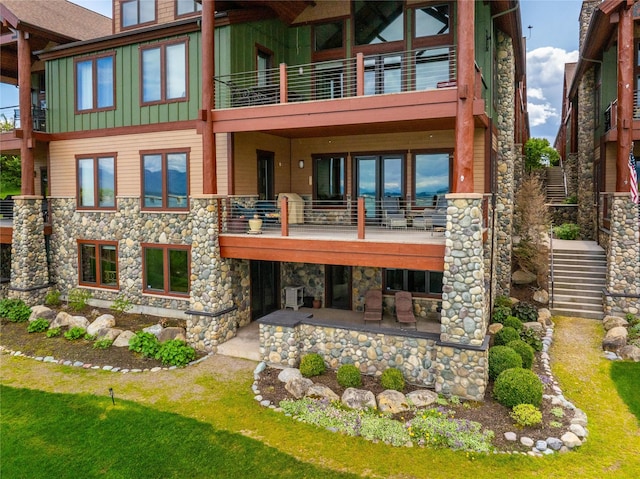 rear view of house with a patio, a balcony, stone siding, stairway, and board and batten siding