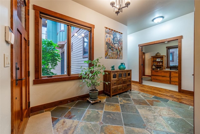 corridor with stone tile flooring, a healthy amount of sunlight, baseboards, and an inviting chandelier