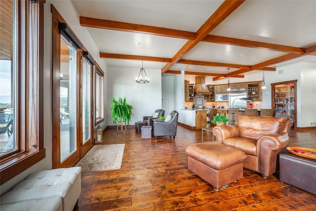 living area with a healthy amount of sunlight, dark wood-style floors, a notable chandelier, and beamed ceiling