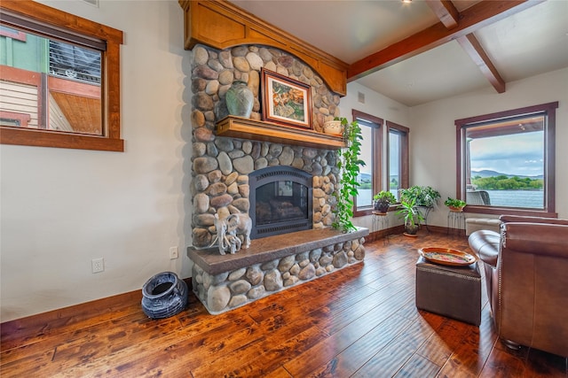 living room featuring beamed ceiling, a stone fireplace, baseboards, and hardwood / wood-style flooring