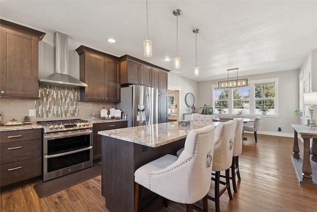 kitchen featuring dark wood-type flooring, a kitchen island, wall chimney exhaust hood, and appliances with stainless steel finishes