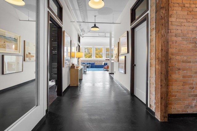 hallway featuring baseboards, concrete floors, and brick wall