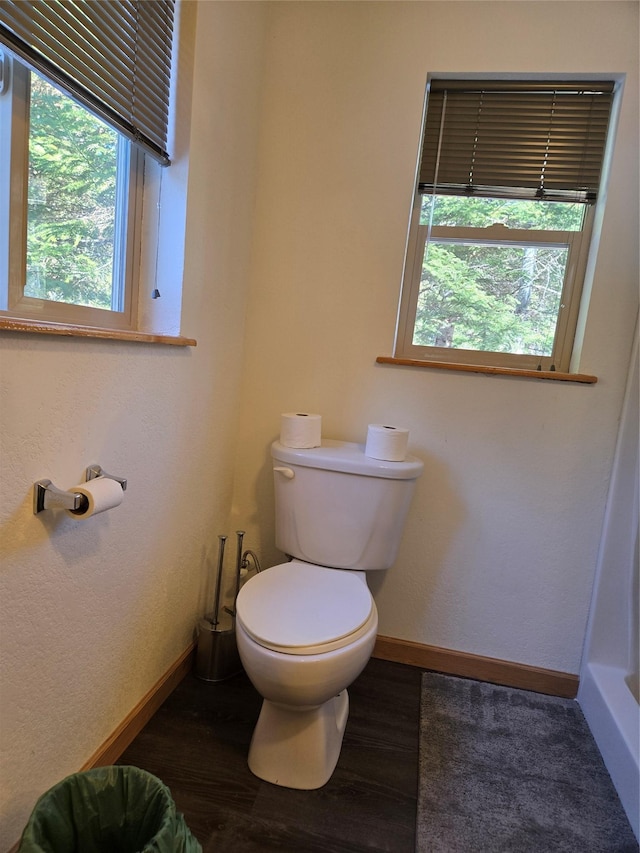 bathroom with baseboards, wood finished floors, toilet, and a healthy amount of sunlight