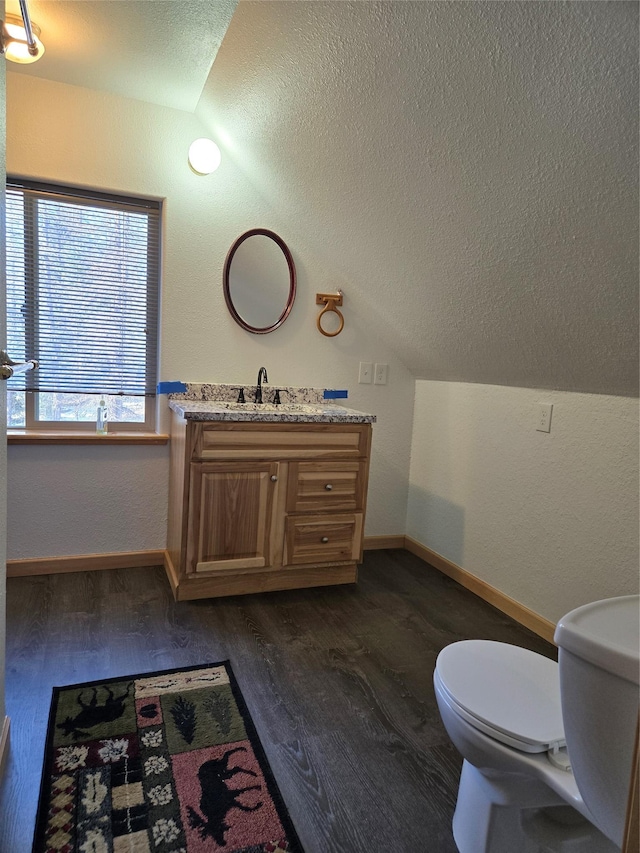 half bath with lofted ceiling, a textured ceiling, toilet, and wood finished floors