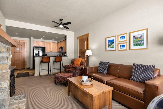 carpeted living room featuring a ceiling fan, a stone fireplace, and a textured ceiling