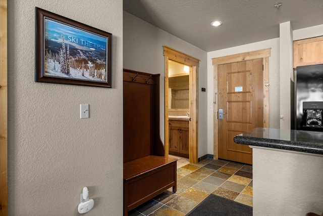 interior space featuring stone tile floors, baseboards, a textured wall, a textured ceiling, and vanity