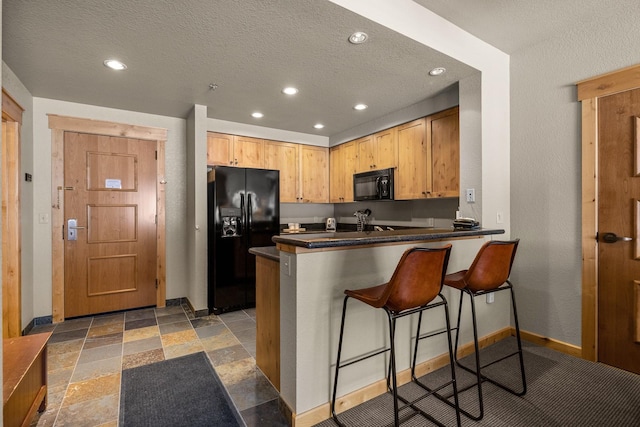 kitchen featuring a breakfast bar, stone tile floors, black appliances, a peninsula, and baseboards