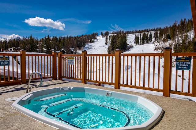 snow covered pool featuring a forest view, a community hot tub, and a wooden deck