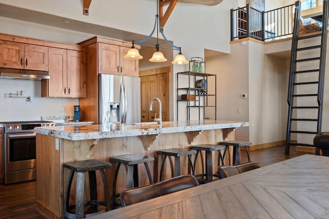 kitchen with light stone counters, dark wood-type flooring, stainless steel appliances, under cabinet range hood, and a kitchen bar