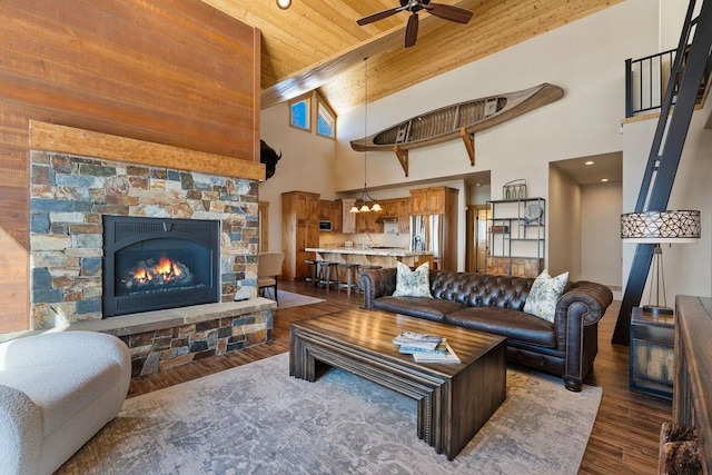 living area featuring ceiling fan, a high ceiling, a fireplace, wood finished floors, and wood ceiling