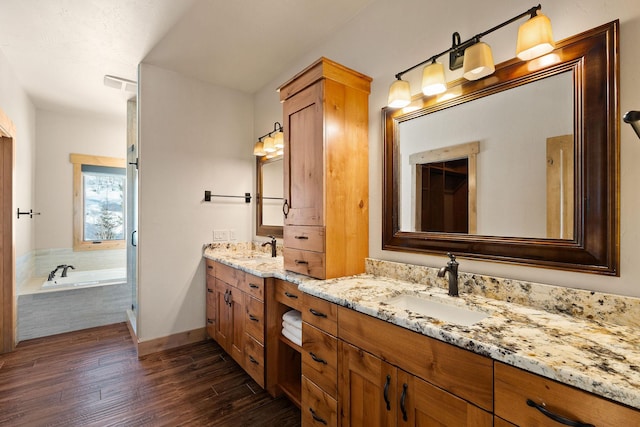 full bathroom with a sink, two vanities, wood finished floors, and a bath