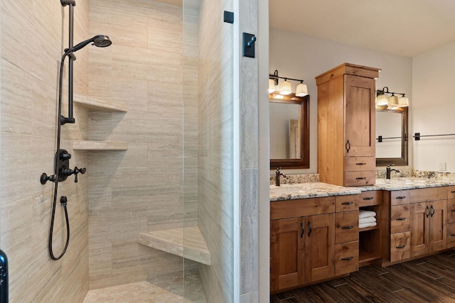 bathroom featuring double vanity, a sink, tiled shower, and wood finished floors