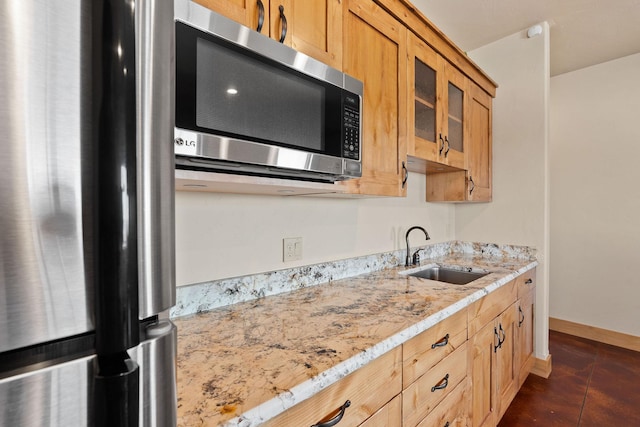 kitchen featuring baseboards, glass insert cabinets, appliances with stainless steel finishes, light stone countertops, and a sink