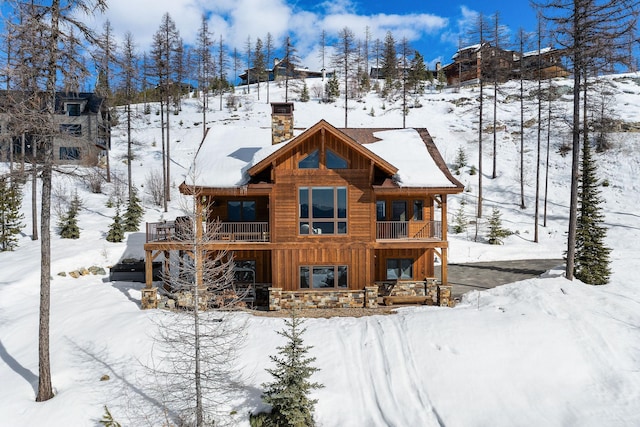 snow covered house with a balcony, a chimney, and board and batten siding