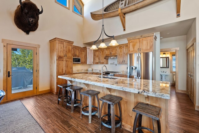 kitchen with under cabinet range hood, a sink, baseboards, appliances with stainless steel finishes, and dark wood-style floors