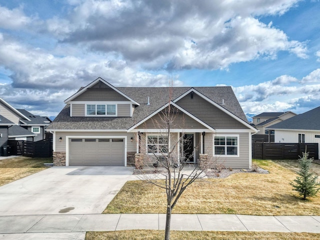 craftsman-style home with fence, driveway, a shingled roof, stone siding, and a garage