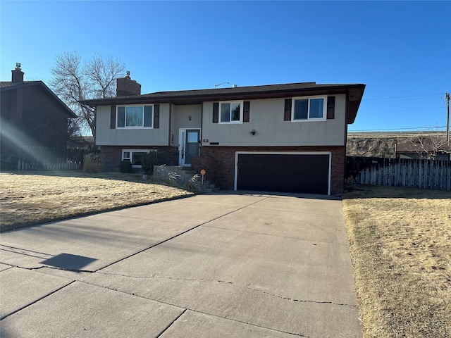 split foyer home featuring brick siding, a chimney, an attached garage, fence, and driveway