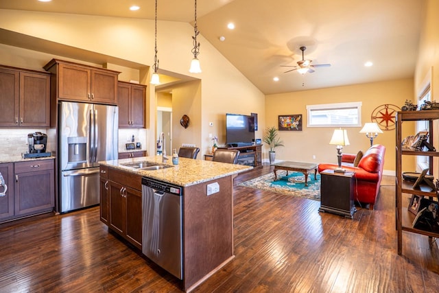 kitchen with light stone counters, dark wood-style flooring, a sink, open floor plan, and appliances with stainless steel finishes