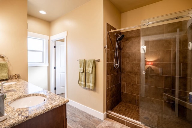 full bathroom featuring wood finished floors, a sink, baseboards, a tile shower, and double vanity