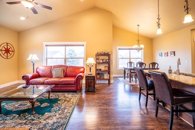 living area with dark wood-style floors, high vaulted ceiling, ceiling fan with notable chandelier, and baseboards