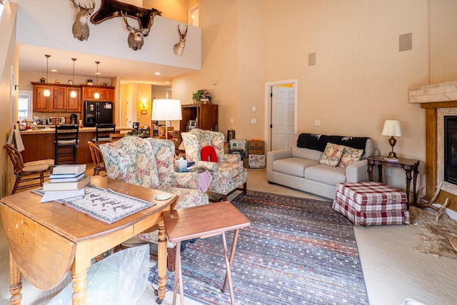 living room with a high ceiling, a glass covered fireplace, visible vents, and light colored carpet