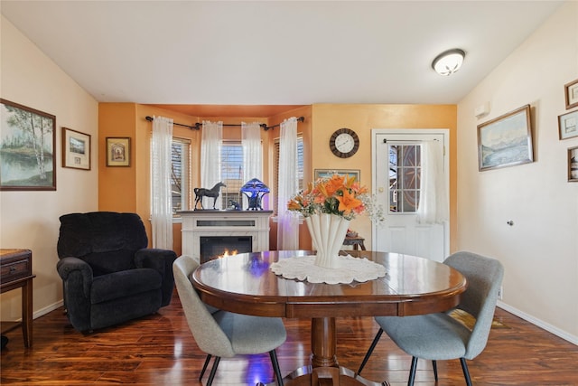 dining space with a lit fireplace, baseboards, and dark wood-type flooring