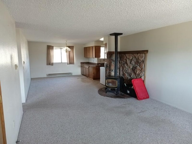 unfurnished living room with a wood stove, light carpet, a baseboard heating unit, and a textured ceiling