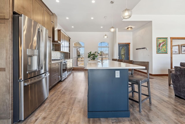 kitchen featuring light countertops, backsplash, appliances with stainless steel finishes, a kitchen island with sink, and wood finished floors