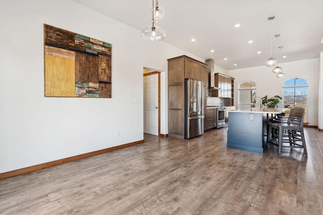 kitchen featuring a center island with sink, baseboards, stainless steel appliances, and wood finished floors