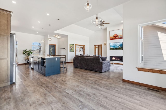 living area featuring visible vents, a glass covered fireplace, ceiling fan, wood finished floors, and baseboards