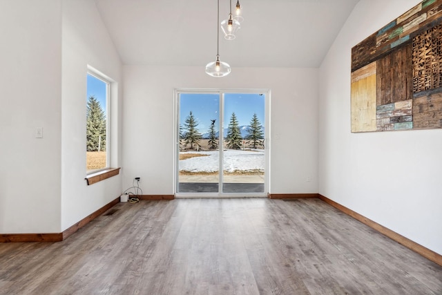 unfurnished dining area featuring baseboards, vaulted ceiling, and wood finished floors