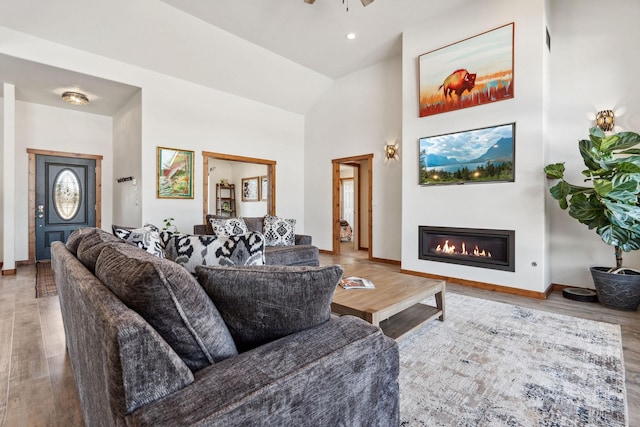 living area with a glass covered fireplace, a towering ceiling, baseboards, and wood finished floors