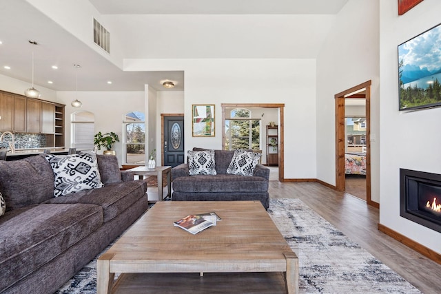 living room with baseboards, visible vents, a glass covered fireplace, a high ceiling, and light wood-style floors