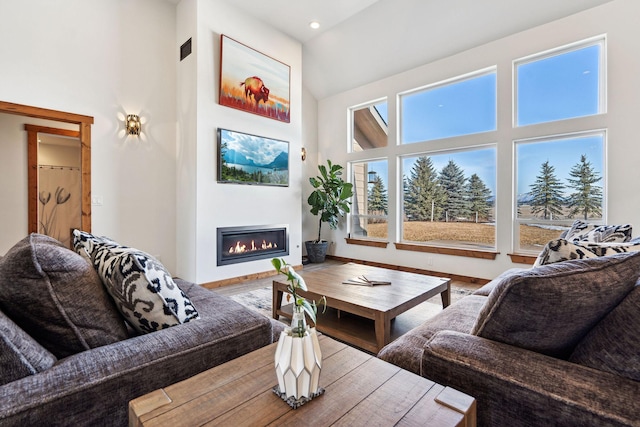 living room with wood finished floors, a glass covered fireplace, a towering ceiling, and baseboards