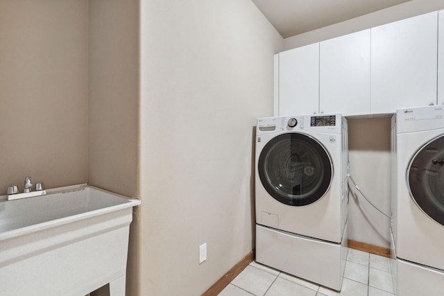 washroom featuring light tile patterned floors, a sink, baseboards, cabinet space, and washer and clothes dryer