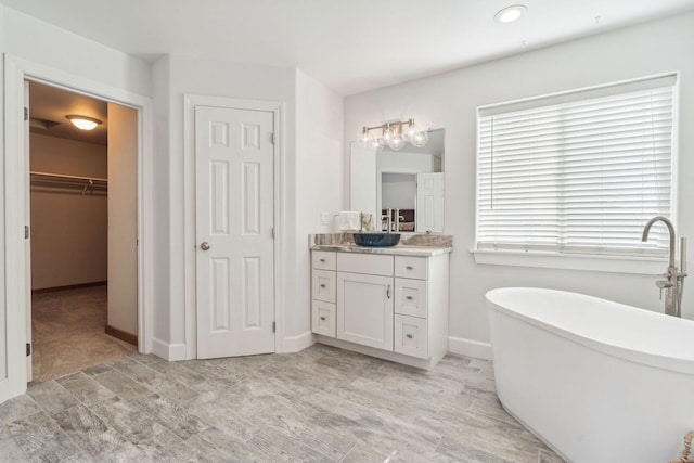 full bath with a freestanding bath, a walk in closet, vanity, and baseboards