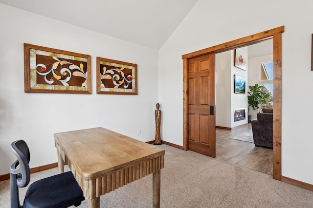 carpeted office featuring lofted ceiling, a glass covered fireplace, and baseboards