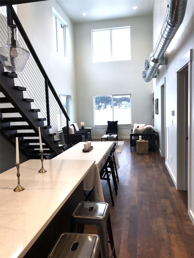 dining space featuring dark wood-style floors, a towering ceiling, baseboards, and stairs