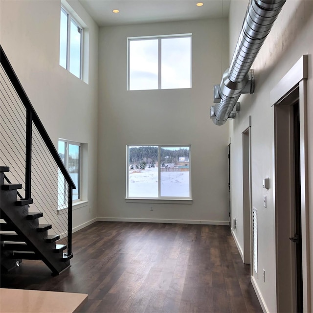 unfurnished living room with dark wood-type flooring, plenty of natural light, and baseboards