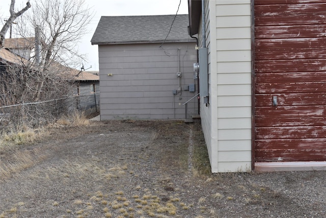 view of side of property with a shingled roof and fence