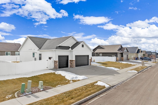 view of front of home with board and batten siding, fence, a residential view, concrete driveway, and stone siding