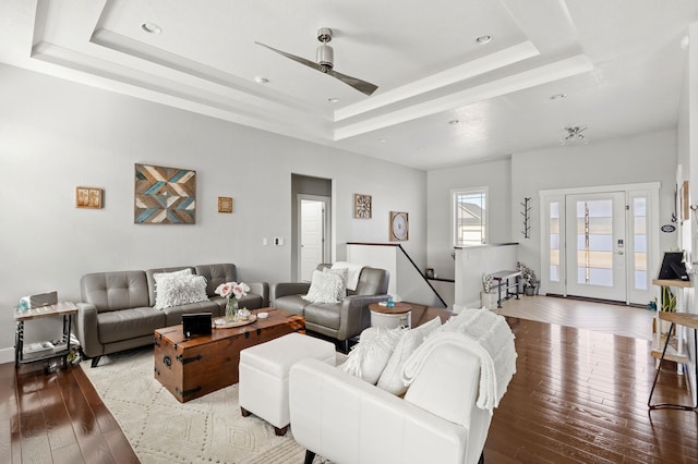 living room with ceiling fan, a tray ceiling, and hardwood / wood-style flooring