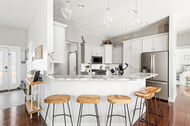 kitchen with white cabinets, appliances with stainless steel finishes, a peninsula, and dark wood-style flooring