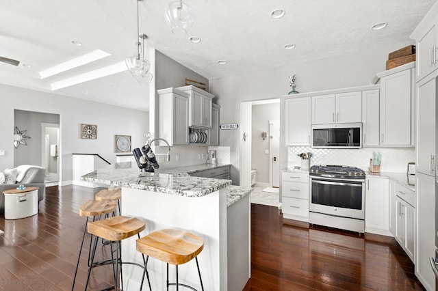 kitchen featuring light stone counters, dark wood finished floors, a peninsula, a breakfast bar area, and gas range