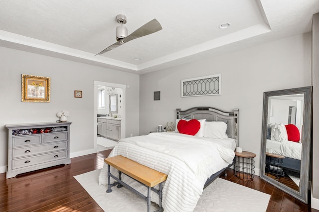 bedroom with a ceiling fan, baseboards, hardwood / wood-style flooring, ensuite bathroom, and a raised ceiling