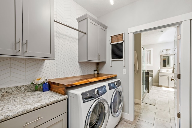 laundry area with light tile patterned floors, baseboards, cabinet space, separate washer and dryer, and a sink