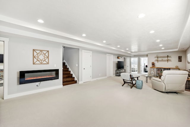 carpeted living room with stairway, baseboards, a tray ceiling, recessed lighting, and a glass covered fireplace