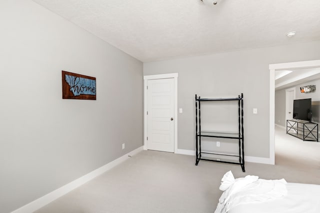 unfurnished bedroom featuring light carpet, a textured ceiling, and baseboards