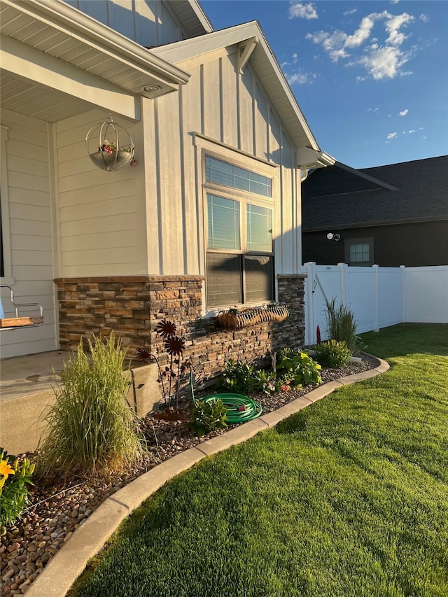 view of side of property featuring fence, a lawn, board and batten siding, and stone siding