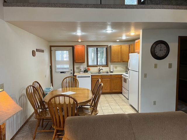 kitchen with white appliances, light tile patterned floors, brown cabinetry, a sink, and light countertops